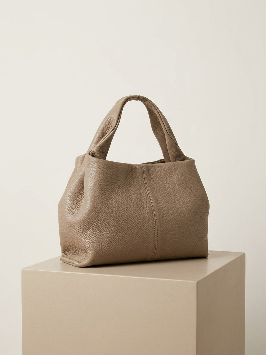 Taupe leren handtas Valentina in premium studio setting met gold hardware en zachte structuur, front view.