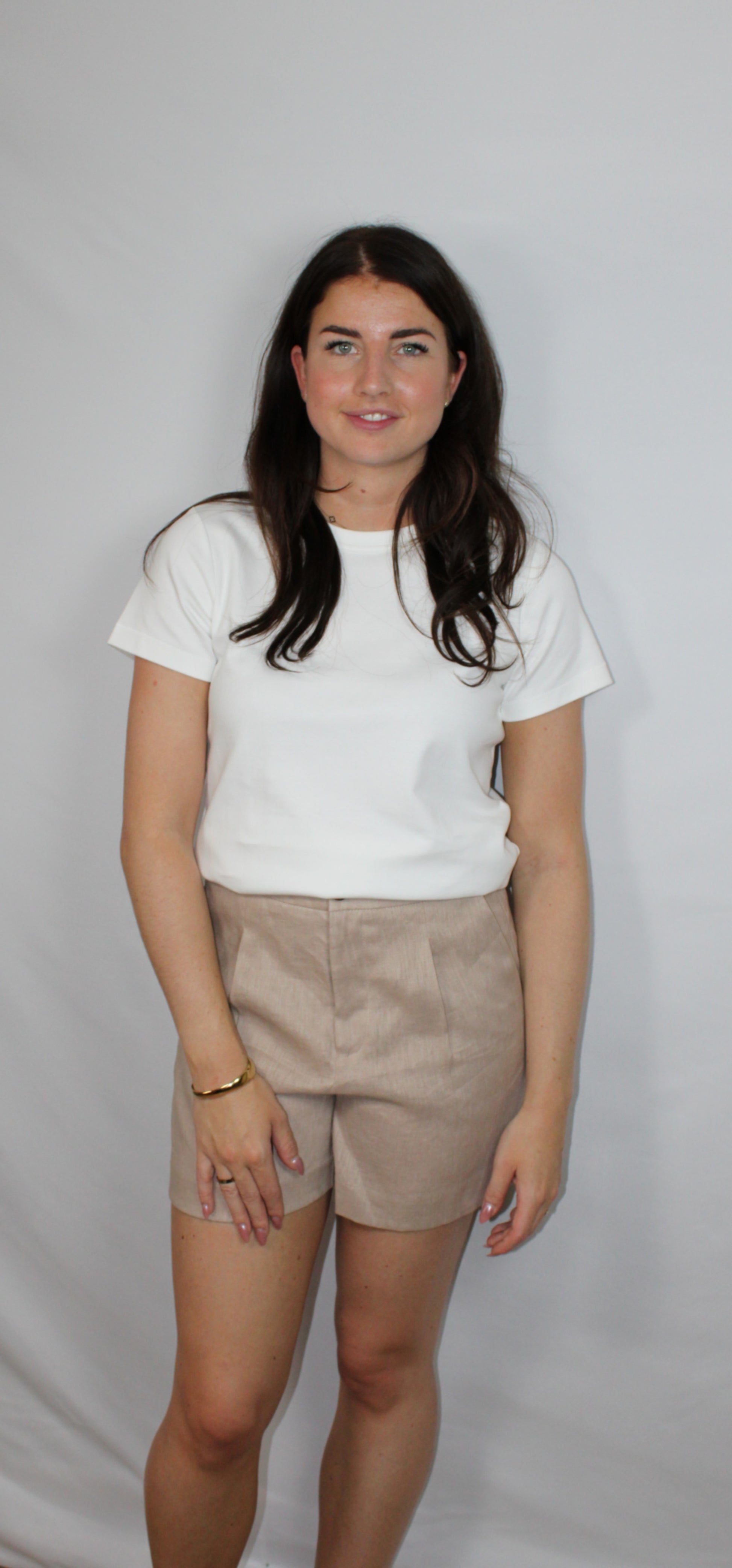 Beige high‑waist linnen short met witte basic top voor dames, 100% linnen, luchtige zomerse pasvorm op lichte studioachtergrond.