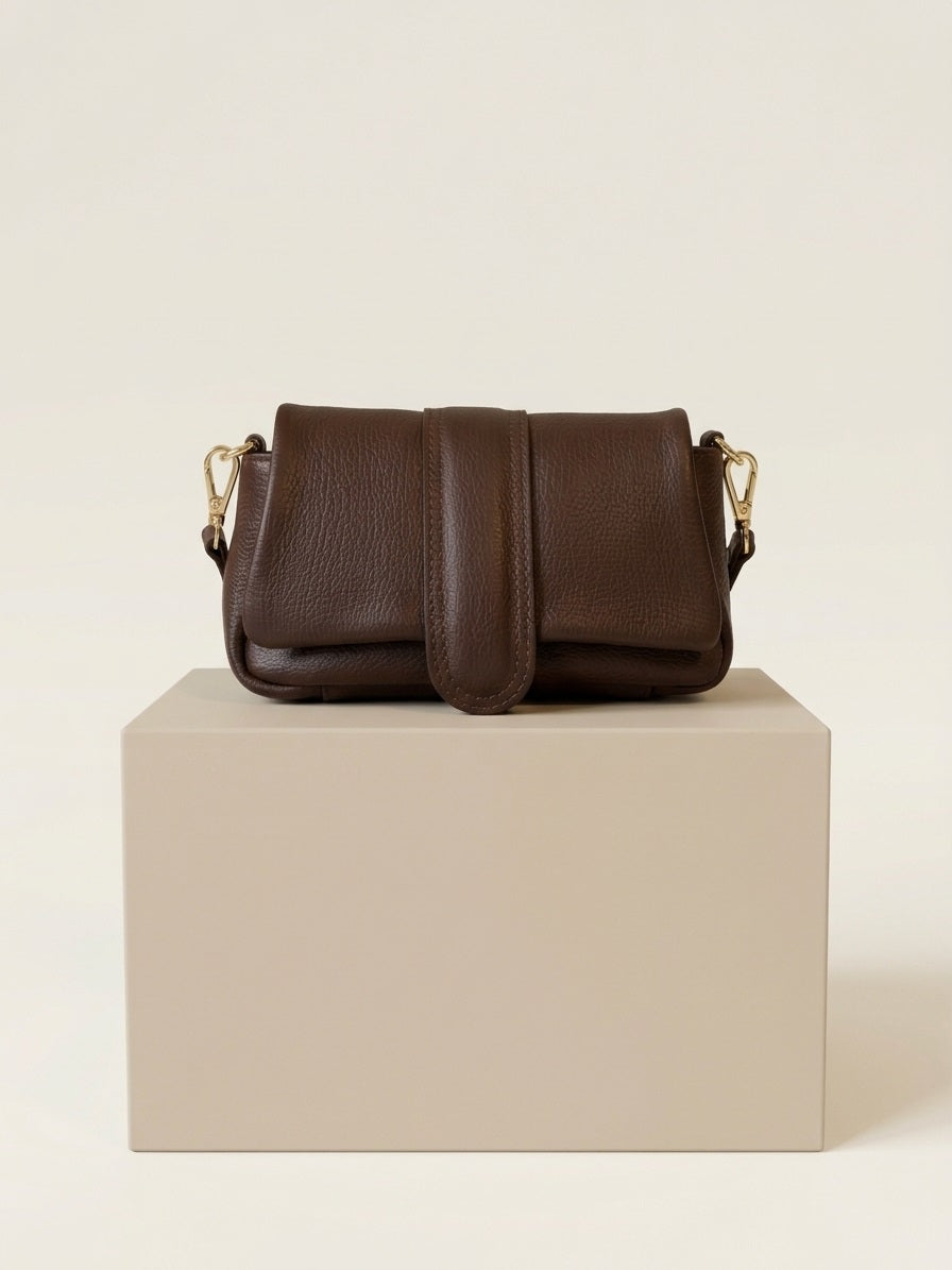 Bruine leren dames handtas gepresenteerd op een beige blok in neutrale studio.