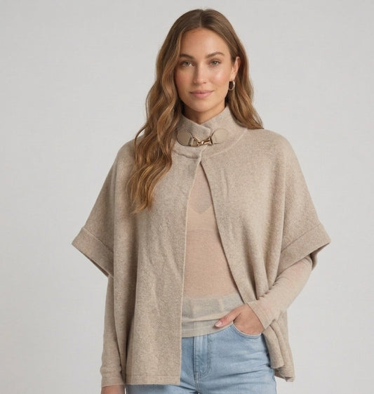 Beige poncho cape dames met licht doorschijnende cashmere top en luxe leder-look gespsluiting.
