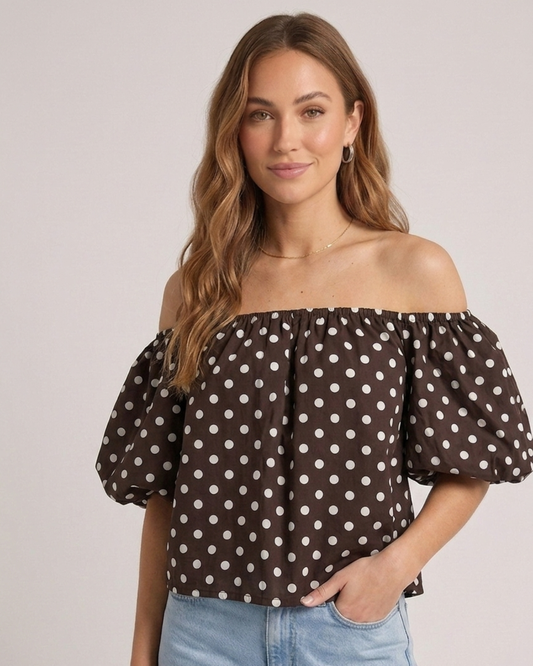 Bruine off shoulder dames top met witte polka dots, gedragen door model in een neutral setting.