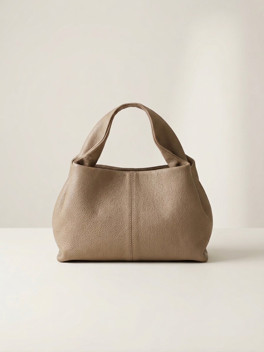 Taupe leren handtas in premium studio setting met gold hardware en zachte structuur, front view.