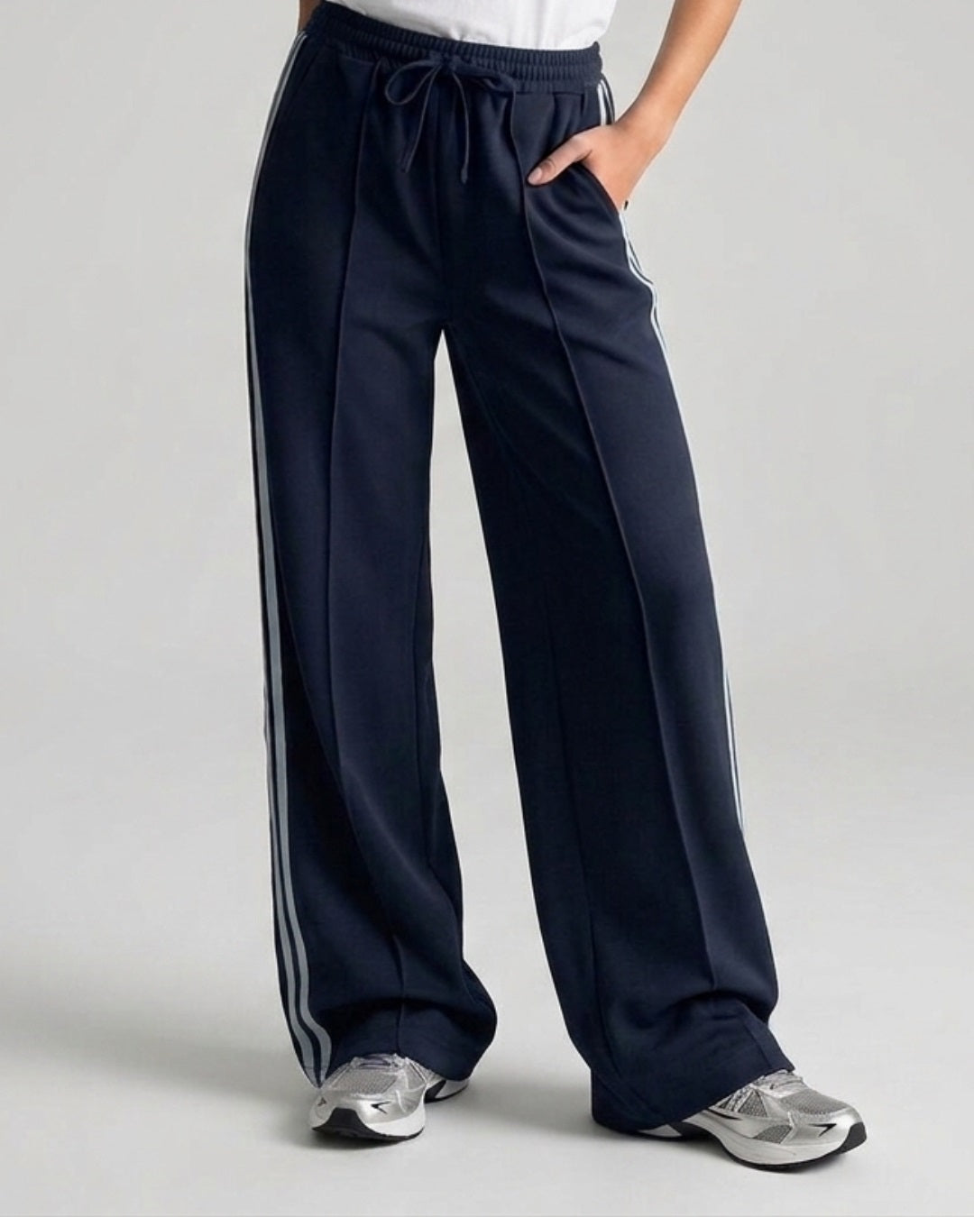 Model draagt een donkerblauwe wide leg broek met lichtblauwe biezen en een elastische taille.