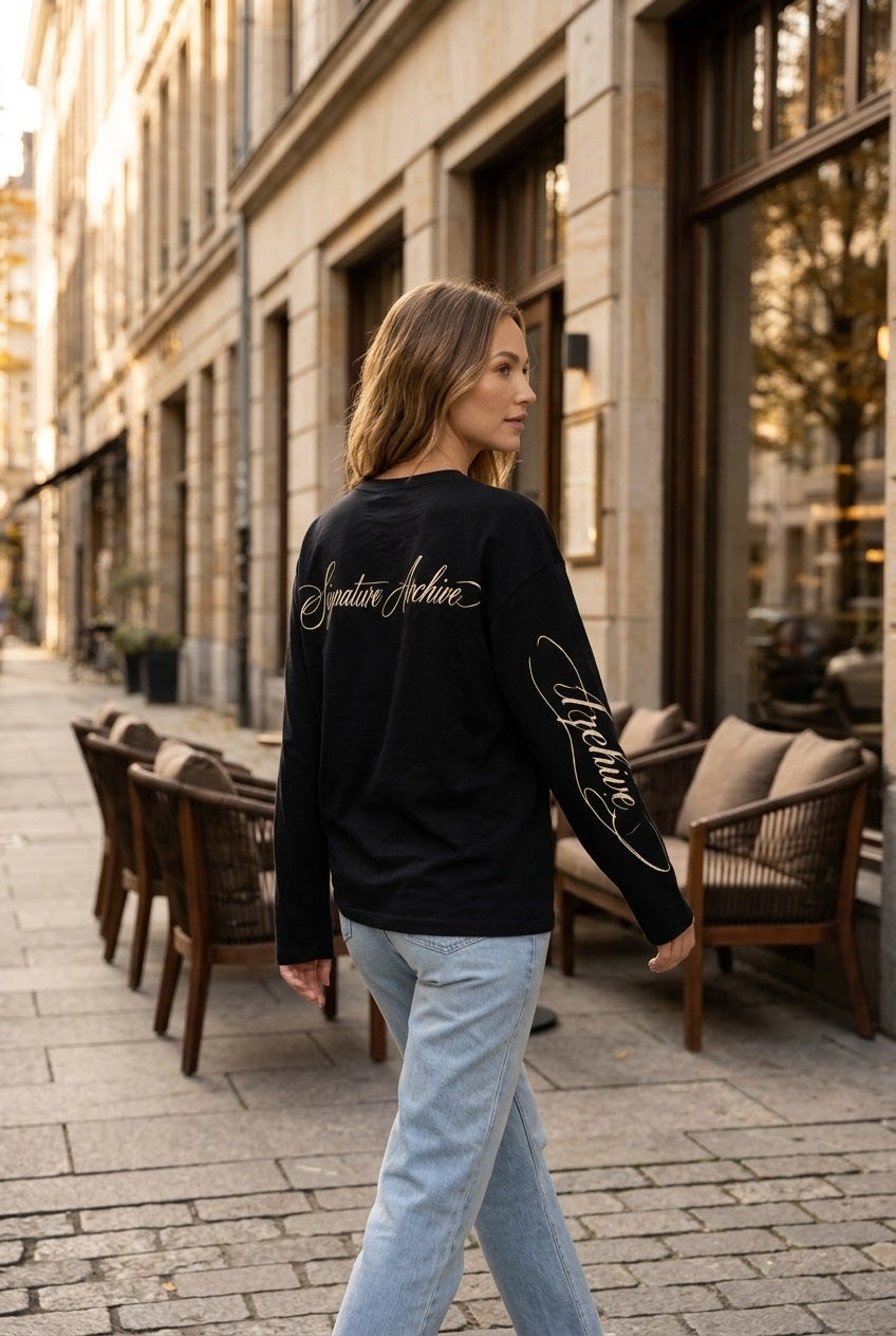 Zwarte statement longsleeve met Signature Archive rugprint en bedrukte mouw gecombineerd met een lichtblauwe jeans tijdens een wandeling door een stijlvolle stadsstraat. Casual chic damesoutfit met een luxe en moderne uitstraling.