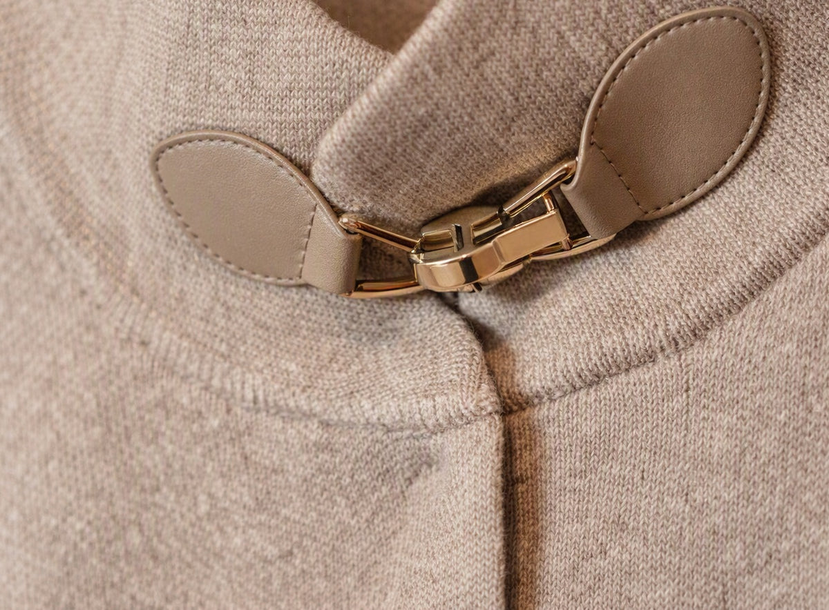 Detail van de goudkleurige gesp en het gebreide materiaal van de beige Lima poncho.