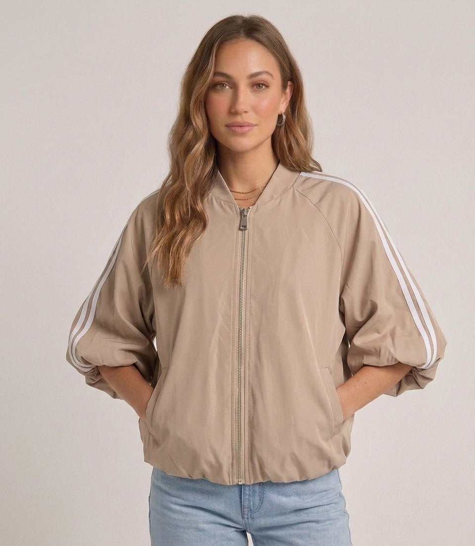 Model draagt het beige track jacket met witte strepen van Myjewellen, een trendy en sportief dames vest voor een minimalistische streetstyle look.