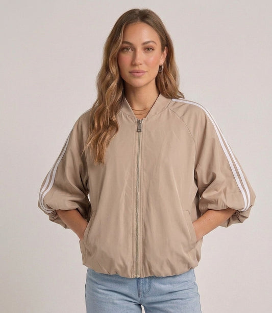 Model draagt het beige track jacket met witte strepen van Myjewellen, een trendy en sportief dames vest voor een minimalistische streetstyle look.