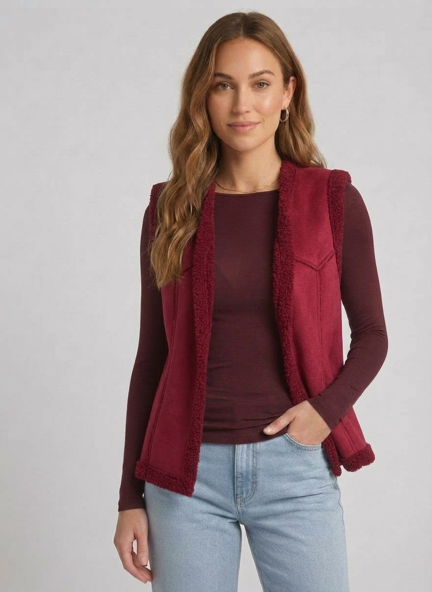 Vrouw draagt bordeauxrode teddy bodywarmer met aubergine top en lichte jeans