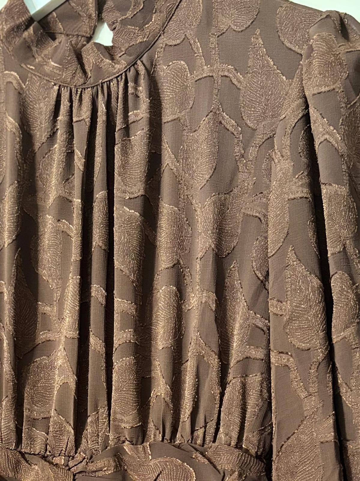 Detailfoto van bruine jurk met jacquard bladstructuur en geplooide halslijn.