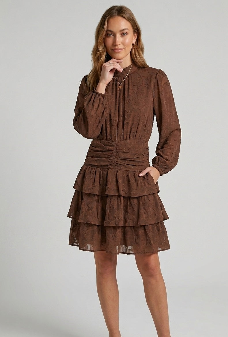 Jurk Soof in het bruin van Myjewellen: een elegante, dubbel gevoerde damesjurk met een hoge hals, gesmokte taille en gelaagde ruches.