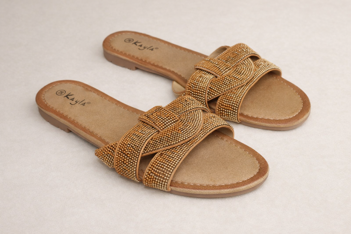 Kayla slippers met dubbele band van gouden rhinestones, gefotografeerd op een zachte neutral beige achtergrond — elegante premium summer look