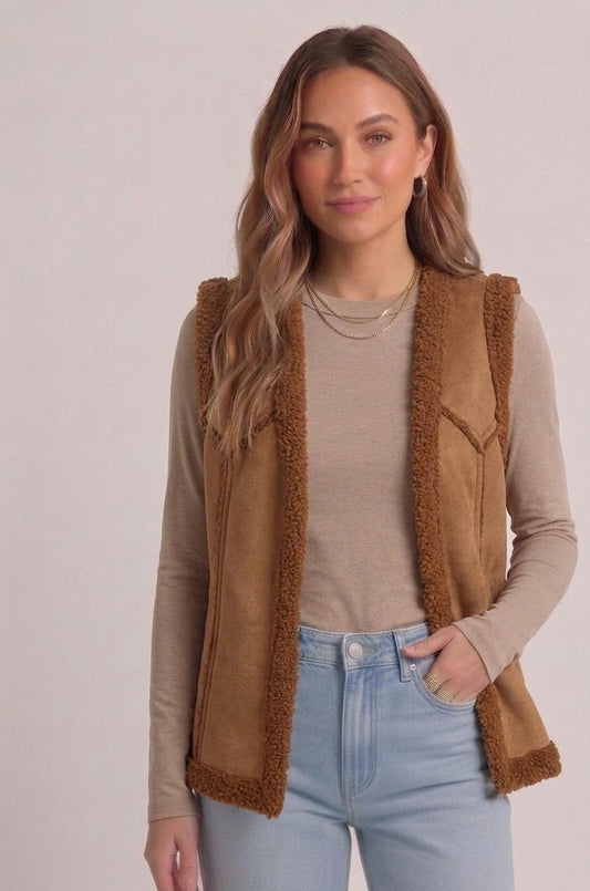 Vrouw draagt camelkleurige teddy bodywarmer met beige top, lichte jeans en gouden kettingen