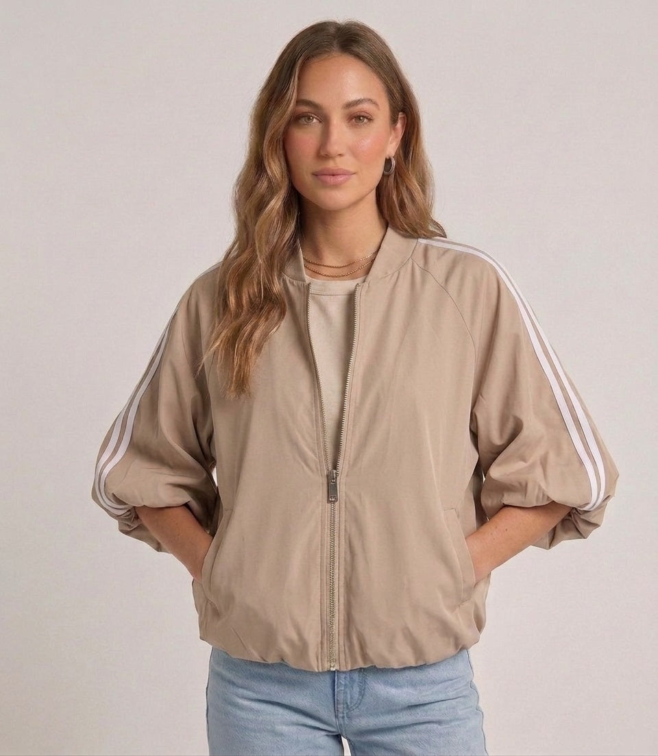 Gedetailleerde productfoto van de soepele ritssluiting, de witte strepen en de brede korte mouwen van het beige dames jack.