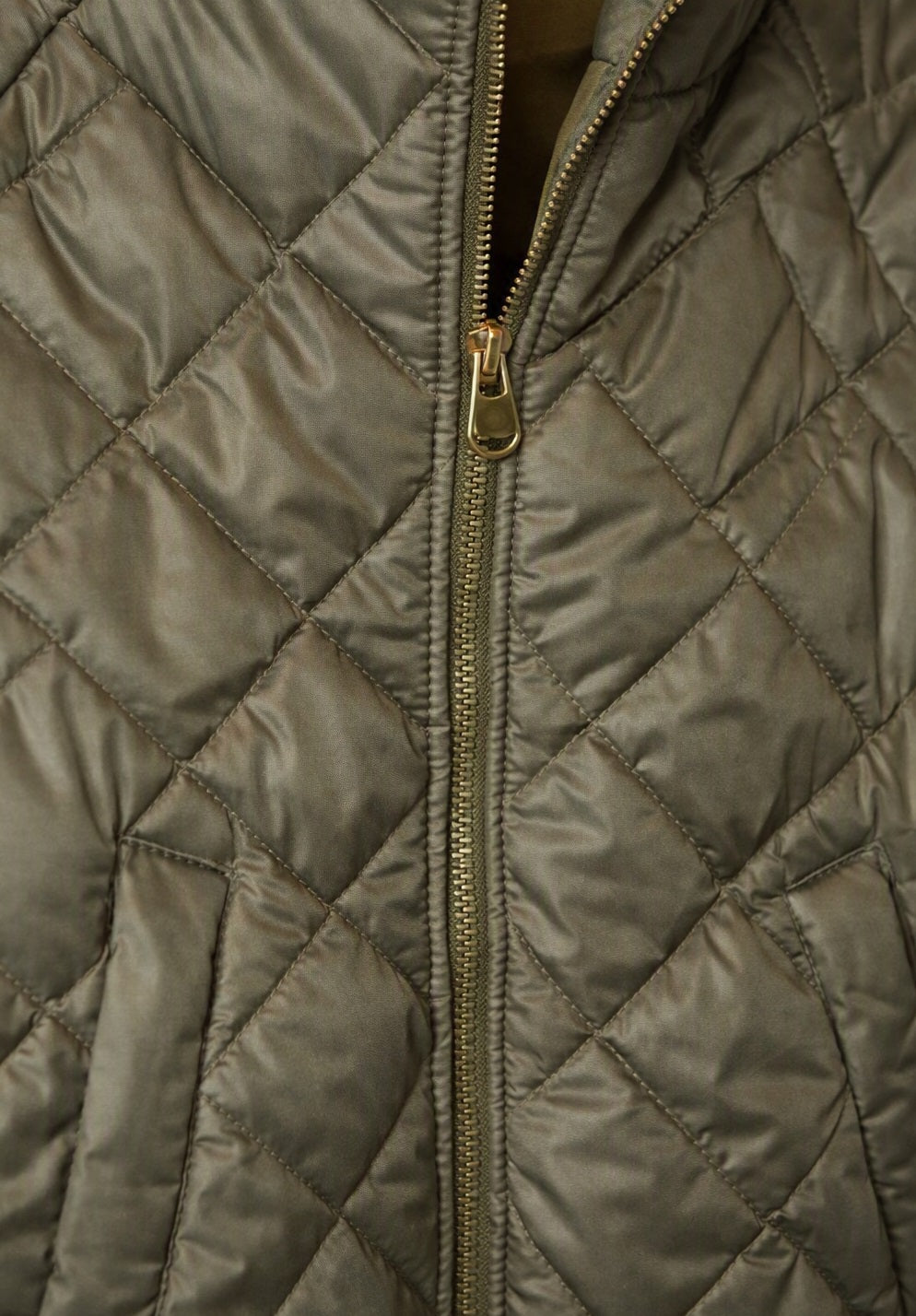 Detailfoto van olijfgroene quilt jas met diamond patroon en gouden rits.