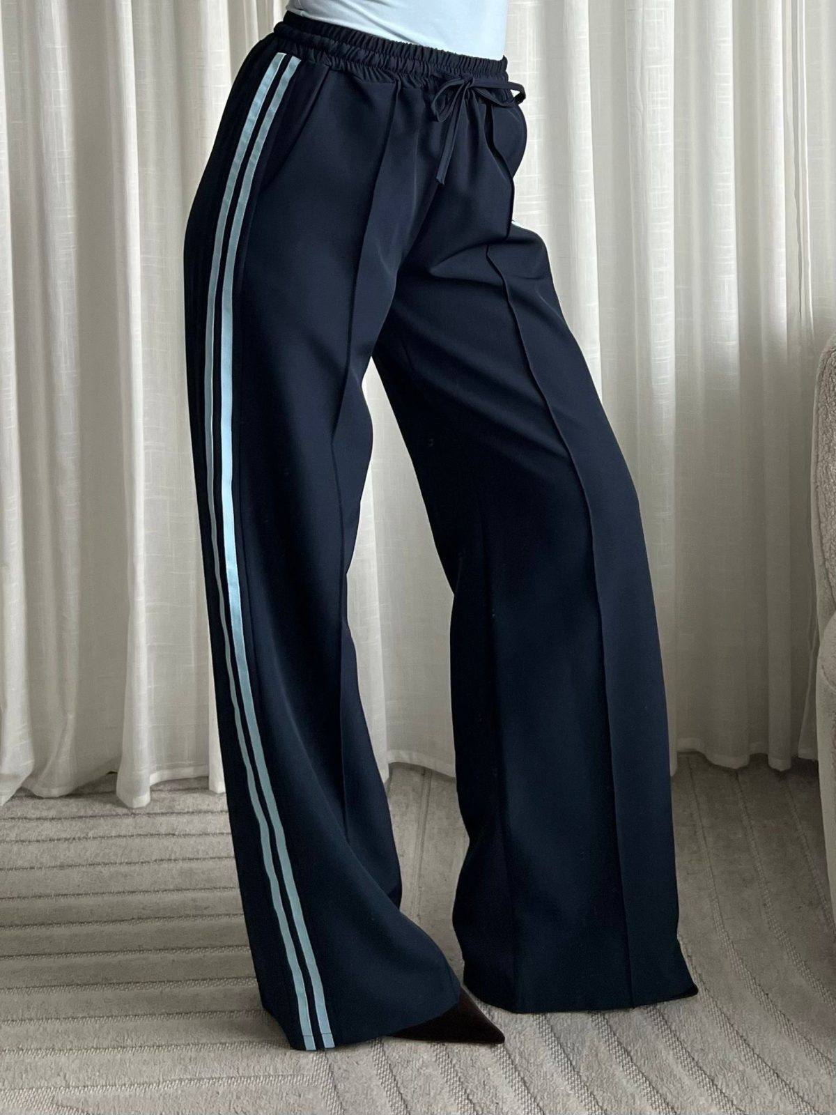 Model draagt een donkerblauwe wide leg broek met lichtblauwe biezen en een elastische taille.