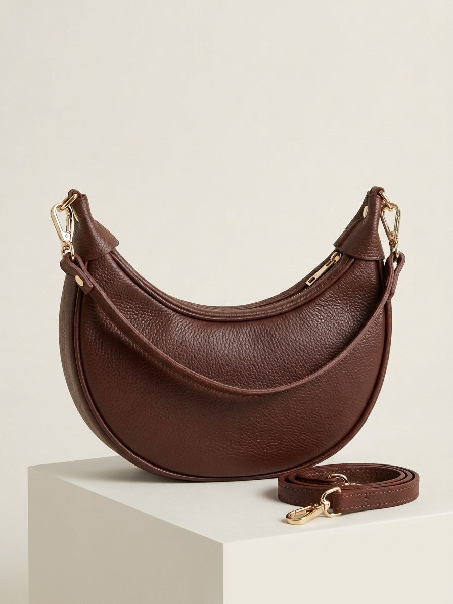 Bruine luxe handtas Emma van echt leer in een minimalistische studio setting.