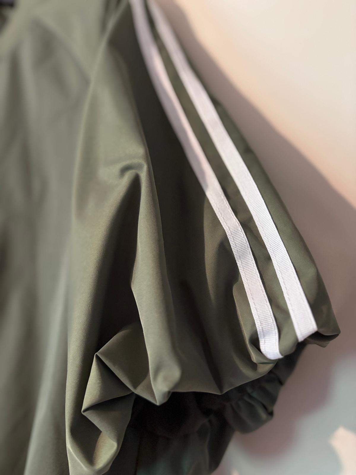 Detailfoto van de sage‑green track jacket met witte strepen op de mouw, close‑up van stof en afwerking.