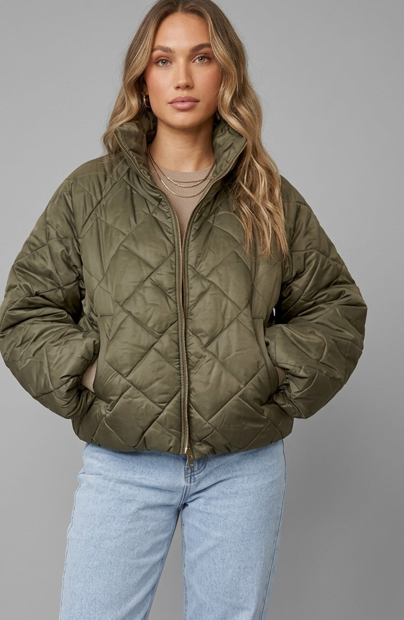 Khaki Puffer Jack Riva van Myjewellen: een trendy olijfgroene gewatteerde damesjas met een doorgestikt ruitpatroon, een hoge opstaande kraag en een gouden rits.