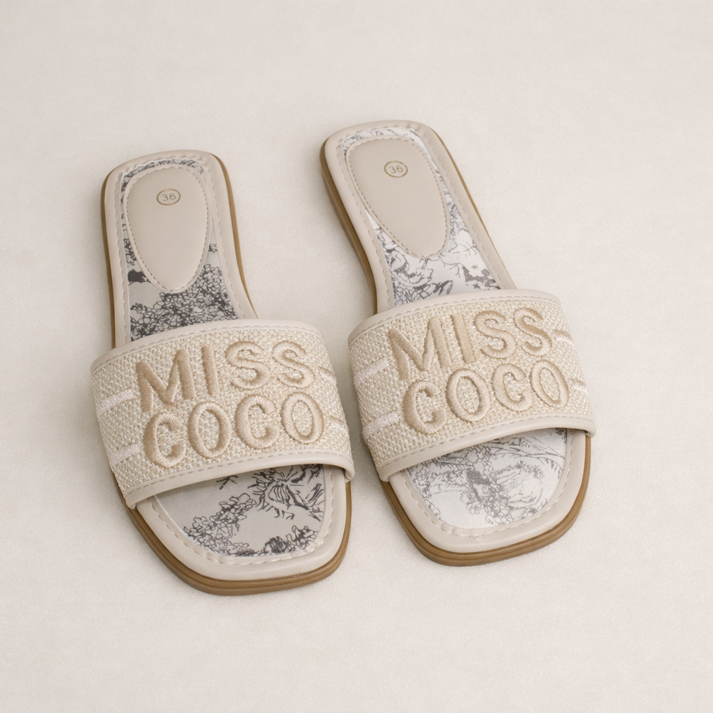 Beige Miss Coco slippers met brede geweven band en subtiele borduring, gefotografeerd op een zachte neutral beige achtergrond — minimalistische premium summer look.