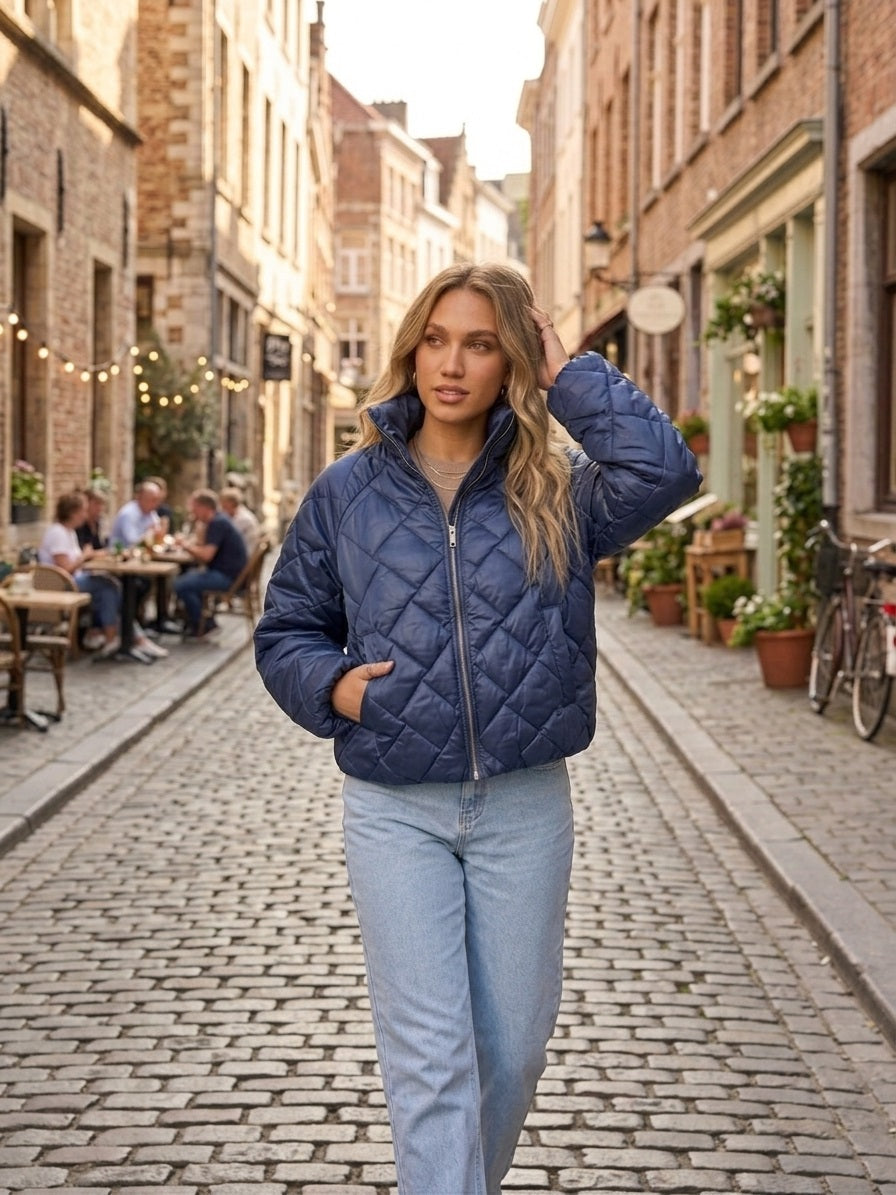 Model draagt navy quilted jacket van Myjewellen in een Europese straatsetting met lichtblauwe jeans.