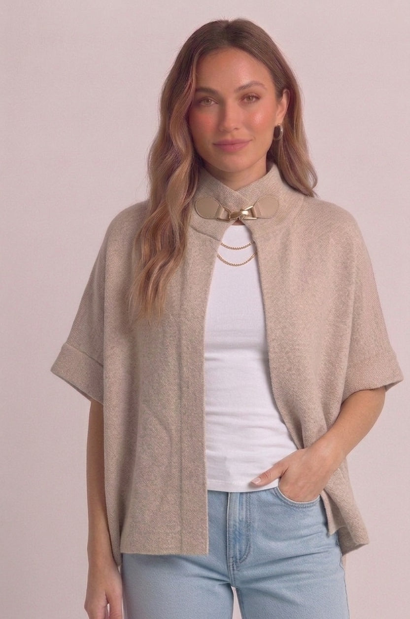 Lima Cape Poncho in het beige van Myjewellen: een luxe gebreid dames cape vest met een opstaande kraag en een stijlvolle gespsluiting.
