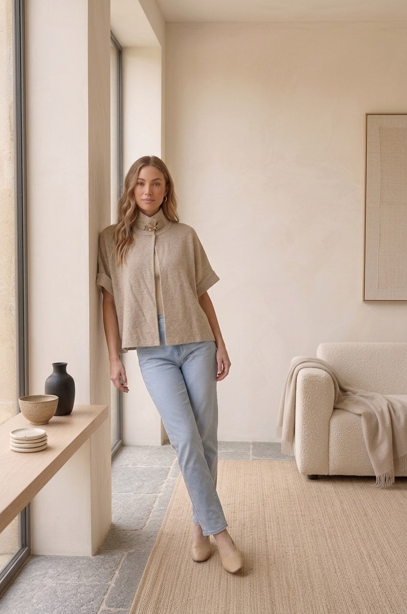 Model draagt de beige gebreide Lima cape poncho op een lichte jeans.
