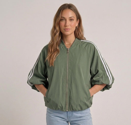 Model draagt het saliegroene track jacket met witte strepen van Myjewellen, een trendy en sportief dames vest voor een minimalistische streetstyle look.