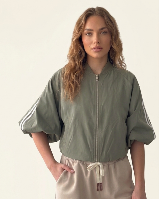 Model draagt het saliegroene track jacket met witte strepen van Myjewellen, een trendy en sportief dames vest voor een minimalistische streetstyle look.