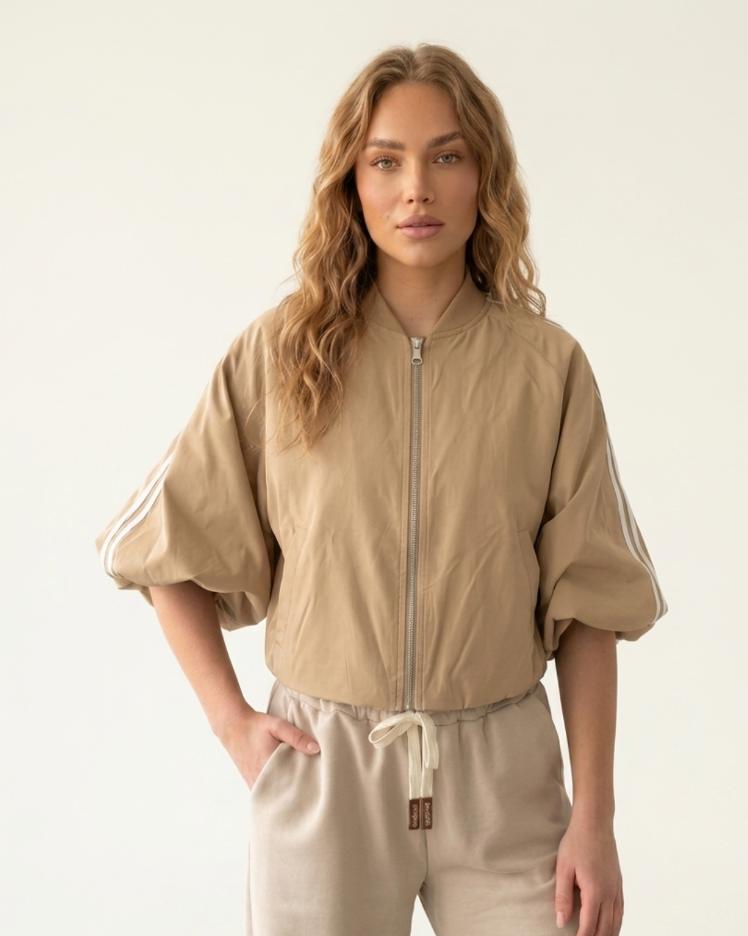 Model draagt een beige zip‑up track jacket met witte strepen