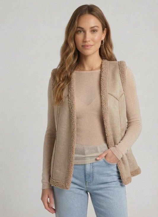 Vrouw draagt beige kleurige teddy bodywarmer met lichte jeans en beige top